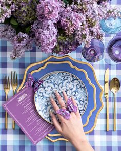 a person's hand on a plate with purple napkins and flowers in the background