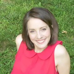 a woman in a red top is laying on the grass and smiling at the camera