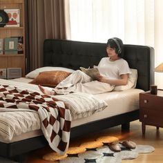 a woman is sitting on her bed reading a book while listening to headphones in the bedroom