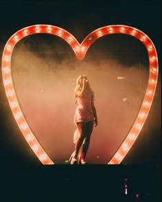 a woman standing in front of a heart shaped sign with lights on it's sides