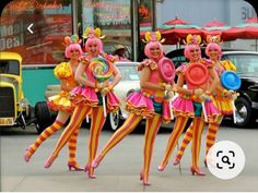 three women dressed in colorful costumes are walking down the street while holding plates and balloons