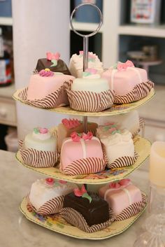 three tiered trays filled with cakes on top of a table next to a candle