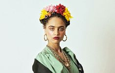 a woman with flowers in her hair wearing a green dress and gold earrings, standing against a white background