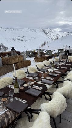 a long table set up with wine and plates on it in the snow covered mountains