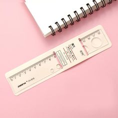 a white ruler sitting on top of a pink surface next to a spiral bound notebook