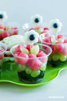 small cups filled with candy and flowers on top of a green platter that is sitting on a table