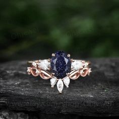 a blue and white diamond ring sitting on top of a piece of wood in front of trees