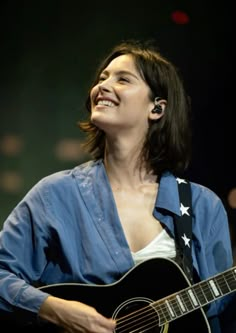 a woman with an american flag on her shirt holding a guitar and singing into the microphone