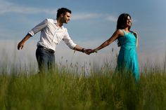 a man and woman holding hands walking through tall grass