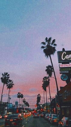 cars are driving down the street in front of some palm trees and buildings at dusk