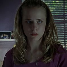 a woman with long blonde hair and blue eyes in a purple shirt looking at the camera