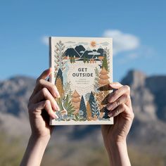 someone holding up a card with the words get outside on it in front of mountains