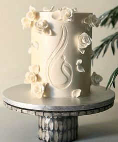 a white wedding cake decorated with flowers on a silver platter next to a plant