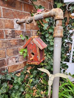 a birdhouse hanging from a pipe next to a brick wall