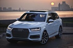 a white car parked in front of a body of water with the sun setting behind it