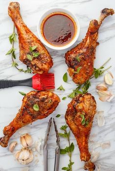 four chicken legs on a marble table with garlic and seasoning next to the wings