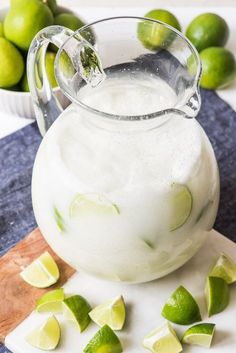 a pitcher filled with limeade sitting on top of a cutting board next to sliced limes