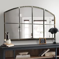 a mirror sitting on top of a wooden table next to a lamp and book shelf