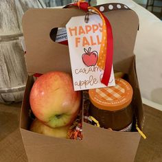 an open box filled with apples and jams on top of a wooden table next to a sign that says happy fall