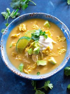 a blue bowl filled with soup and topped with sour cream, avocado and cilantro