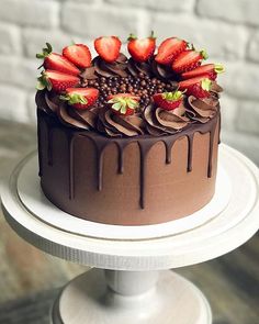 a chocolate cake topped with strawberries on top of a white plate next to a brick wall