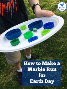 a person holding a tray with plastic cups on it and the words how to make a marble run for earth day