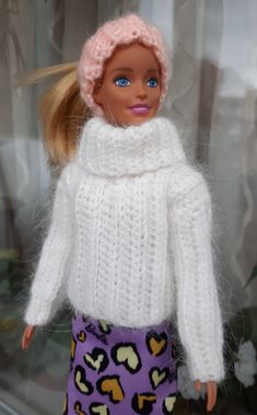 a barbie doll wearing a white sweater and purple skirt with hearts on the bottom, standing in front of a window