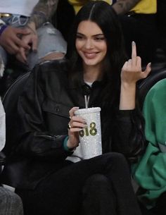 a woman sitting next to a man at a basketball game holding a drink and giving the peace sign