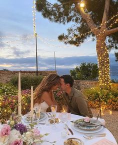 a man and woman sitting at a table in front of a tree with lit candles