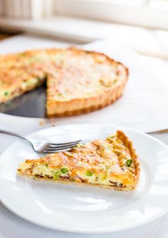 a slice of quiche on a white plate with a fork next to the pie