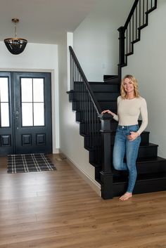 a woman standing in front of a staircase next to a black door and wooden floor