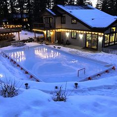 an outdoor swimming pool surrounded by snow covered ground with lights on the side of it