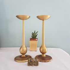 two golden candlesticks and a small potted plant on a white table cloth