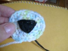 a hand holding a crocheted sheep brooch with a black face on it