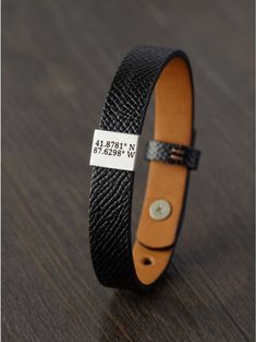 a black and tan leather bracelet with a gold plated nameplate on the clasp