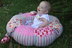 a baby sitting in a pink and red flowered bean bag chair on the grass