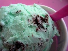 a scoop of green ice cream in a bowl with a pink spoon on the side