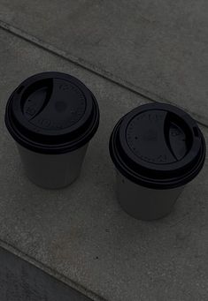 two black coffee cups sitting next to each other on the sidewalk with their lids closed