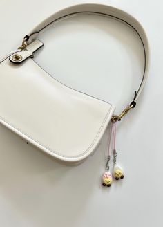 a white purse with two small charms attached to it