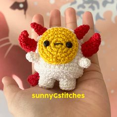 a hand holding a tiny crocheted yellow and white stuffed animal with red wings