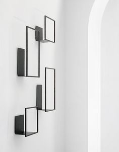 a white wall with four black square shaped shelves on it's sides and one is hanging from the ceiling