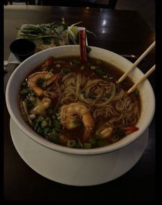 a bowl of soup with shrimp and noodles in it on a table next to chopsticks