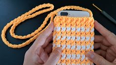 someone is holding an orange and white cell phone case in their left hand, next to a crocheted string