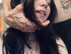 a woman with black hair and tattoos on her arm is holding her hand up to her face