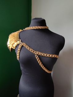 a black mannequin with gold chains and wings on it's back, in front of a green wall