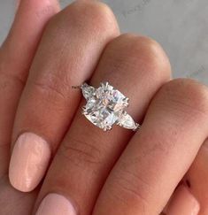 a woman's hand holding an engagement ring with two pear shaped diamonds on it