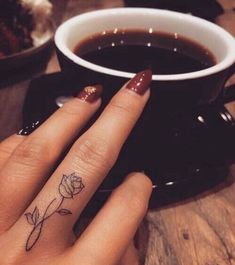 a woman's hand with a small rose tattoo on her ring finger next to a cup of coffee