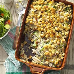 a casserole dish filled with vegetables and bread crumbs next to a bowl of salad