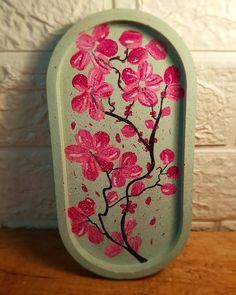 a green tray with pink flowers painted on the front and back of it, sitting on a wooden table