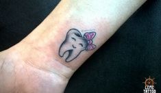 a tooth with a pink bow on it's head is tattooed onto the wrist